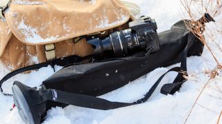 Domke canvas tan coloured camera bag with some snow on lid, left in snow with next to it a tripod bag