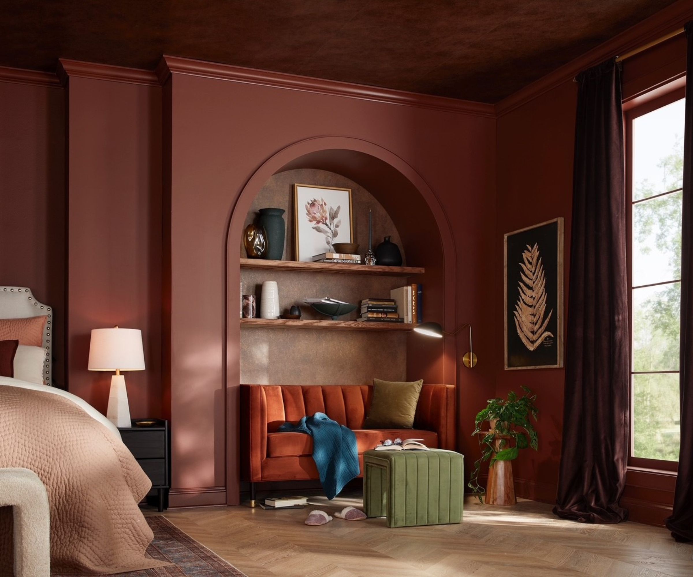 Mahogany red painted bedroom with arched bookshelf and reading nook with orange sofa and green ottoman and large window
