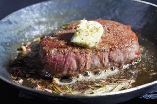 A fried fillet of steak in a pan with a knob of butter