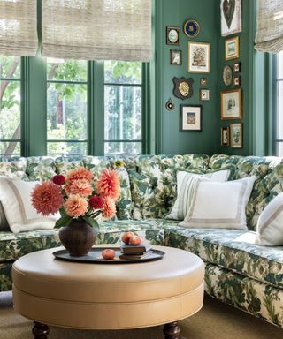 formal living room with green walls, gallery wall, large windows with neutral blinds, floral green corner sofa, circular beige coffee table