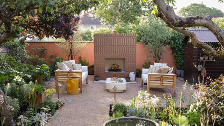 A garden with trees, luscious garden borders, and a seating area and fireplace as a focal point