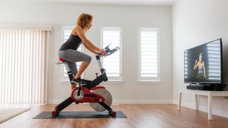 A woman using an exercise bike in her home while watching TV