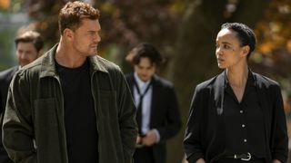 From left to right: Alan Ritchson lookint to his right at Maria Sten who is looking at him. 