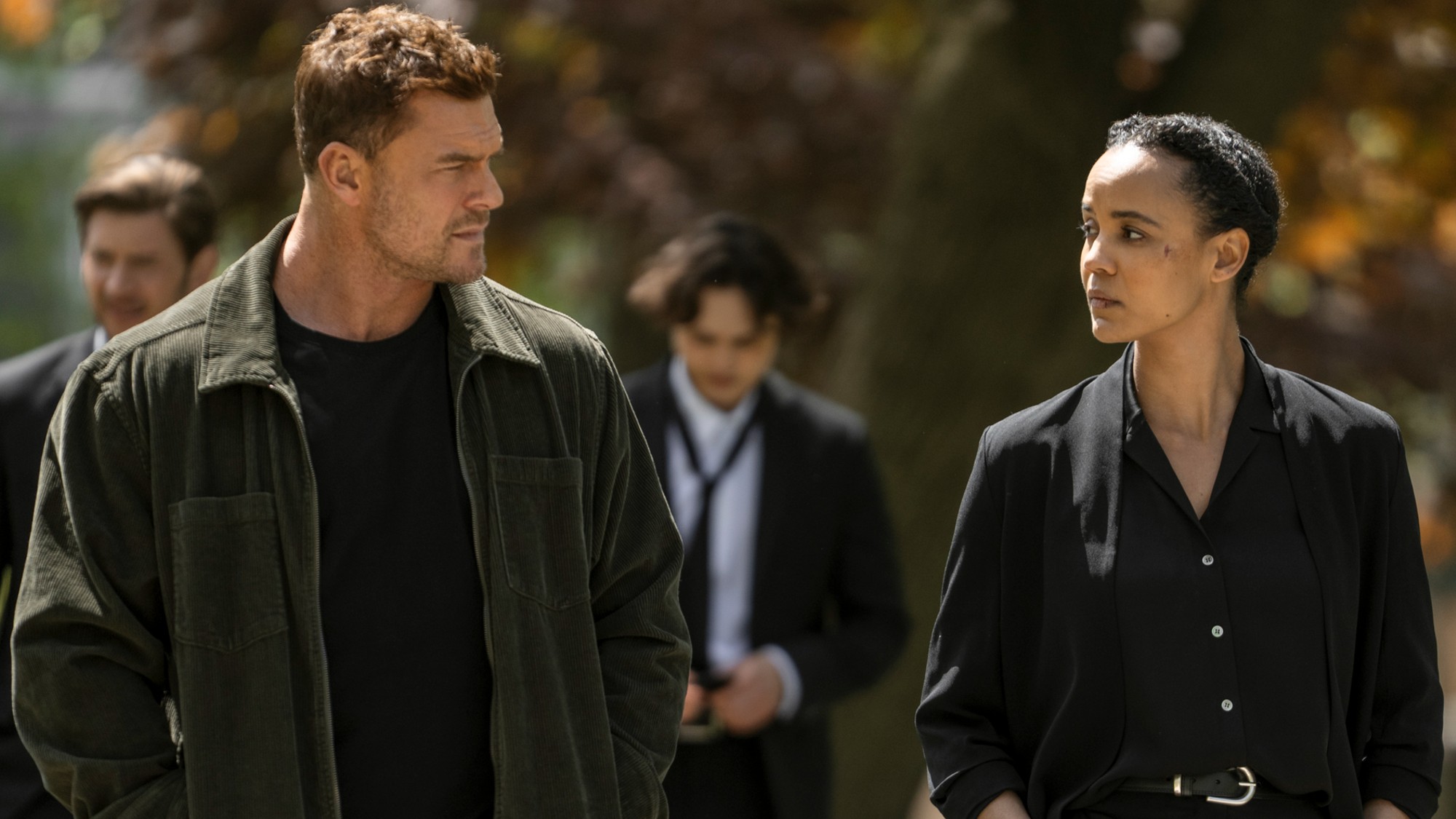 From left to right: Alan Ritchson lookint to his right at Maria Sten who is looking at him. 