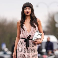 Kelsey Merritt wears black sunglasses, burgundy bordeaux lipstick, light pink sheer mesh knit plugging necklace black bow belt Chanel midi dress