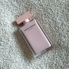 Bird's eye view of a bottle of Narciso Rodriguez For Her laying on a cream boucle fabric background