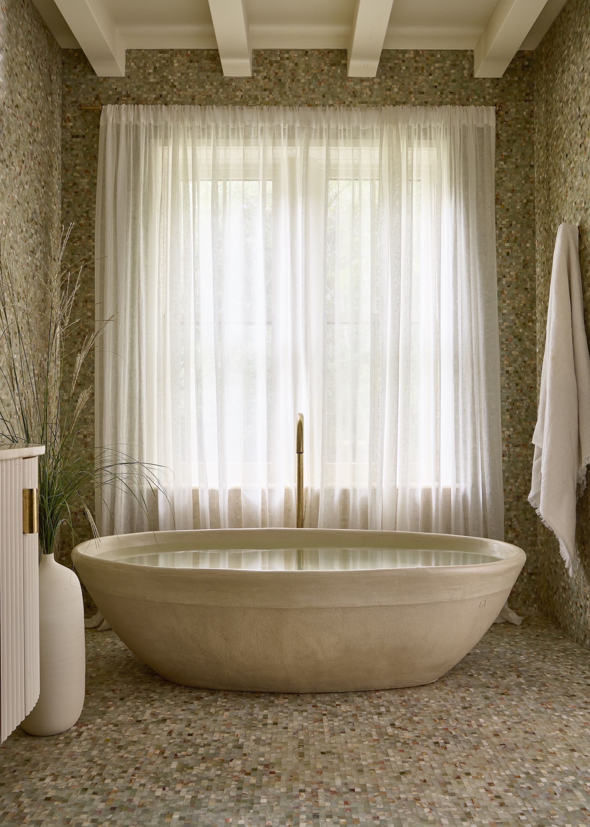 bathroom with mosaic floor and stone bath in the middle of the room. There are also sheer curtains hanging up in the bathroom