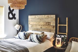 Spare bedroom with supersize wooden pallet headboard against dark navy wall, ladder shelving and rattan pendant light