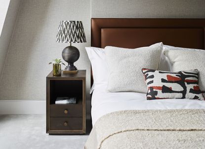 A bedroom with earthy tones, a wooden headboard, beige bed sheets, a cream carpet, and white skirting boards