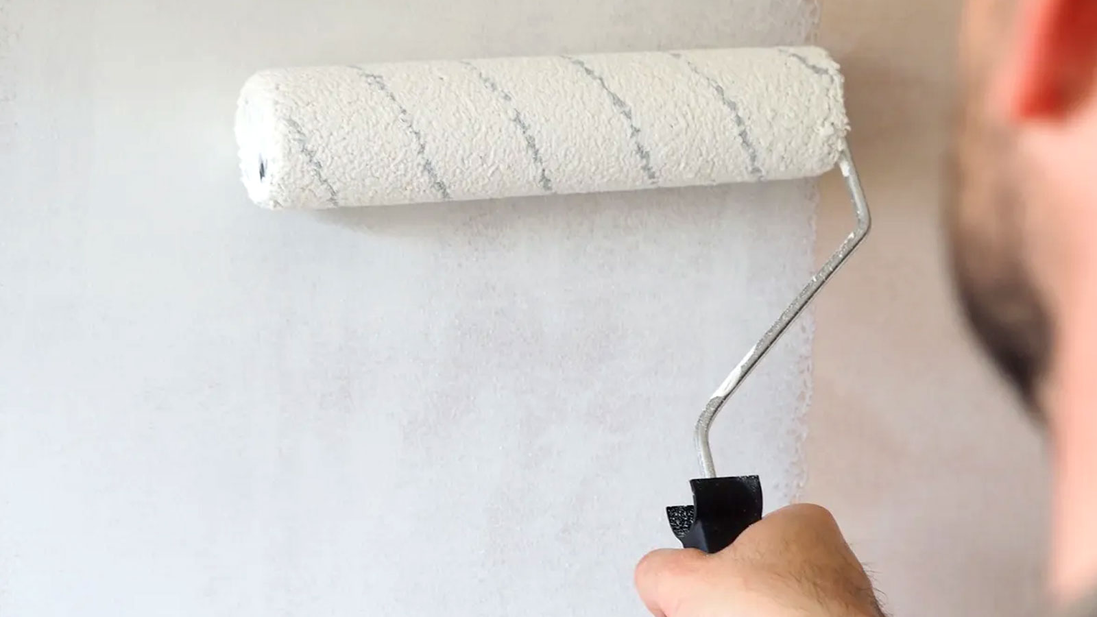 Person painting a white mist coat with a 9 inch roller onto bare plaster