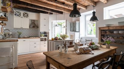 beamed kitchen with white unit and rustic wooden dining table in a stone built french rural house