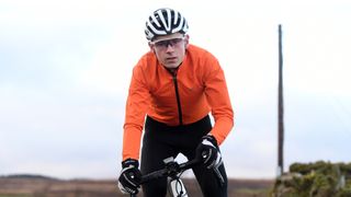 Image shows a rider training in an orange cycling rain jacket.