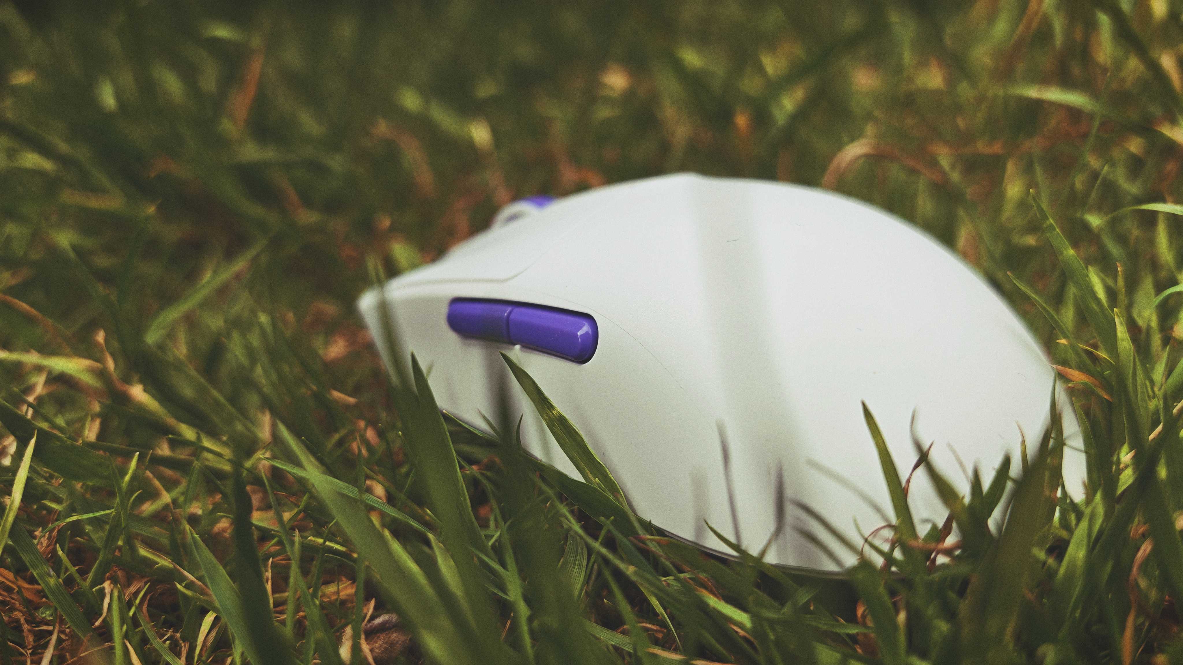 A white and purple Akko Dash Ultra gaming mouse sitting in tall grass in a garden
