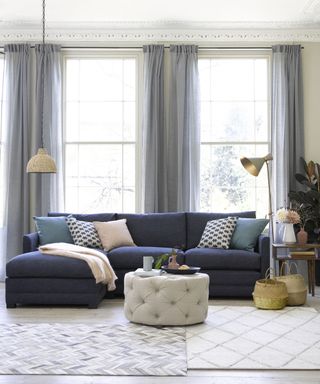 Living room with duo of rugs, buttoned round pouffe, and dark blue sofa with assorted scatter pillows.