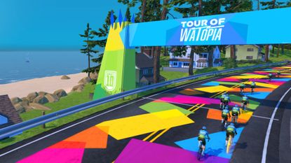 A screengrab of a blue and green arch in Zwift&#039;s Tour of Watopia with riders on a rainbow road beneath it.