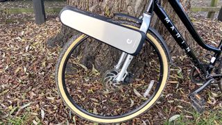 a black city bike is photographed with the CLIP e-bike conversion kit attached to the front wheel