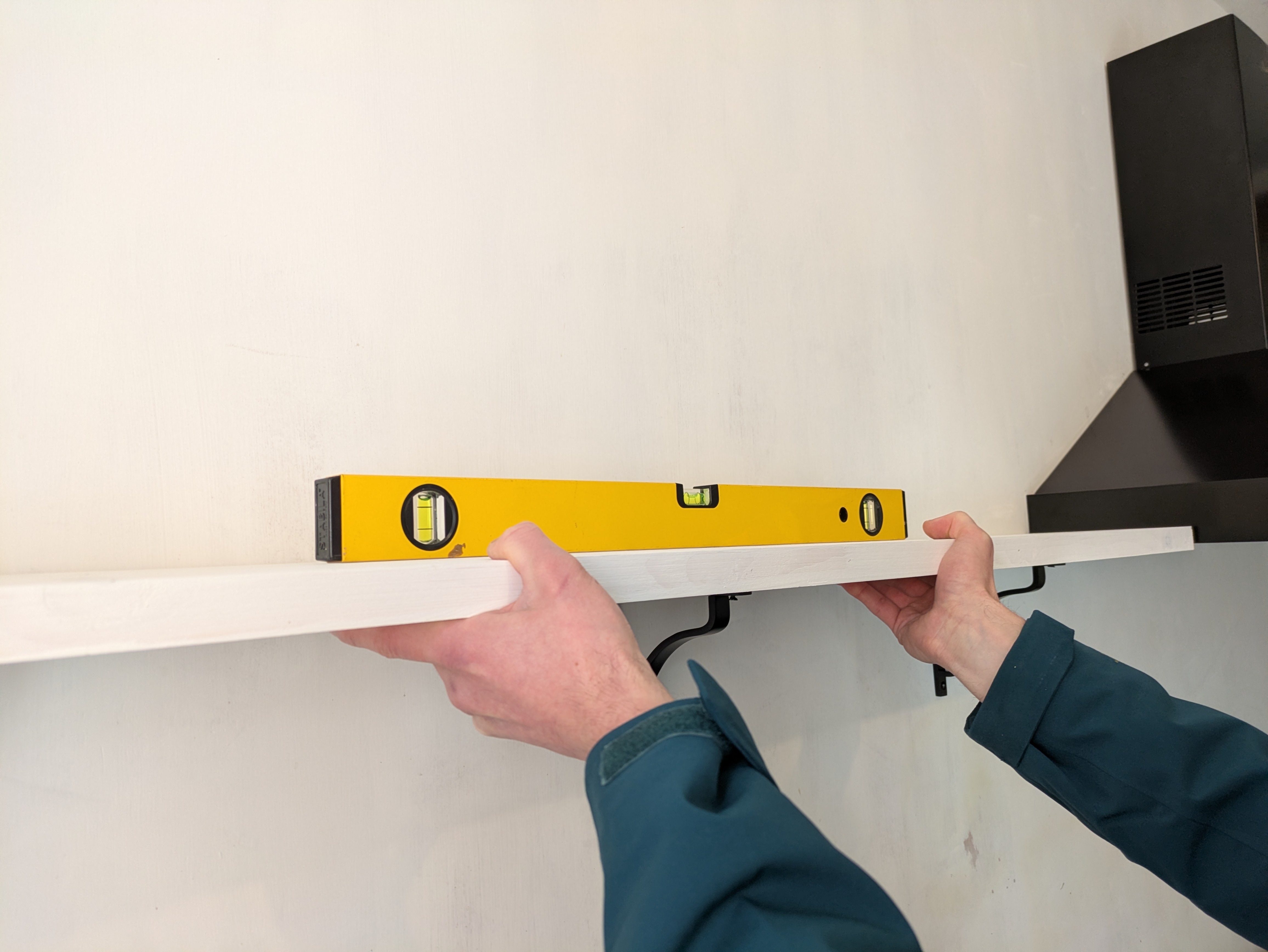 Using a spirit level to check the level of a shelf against a wall