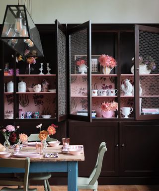 dining room kitchen with large custom cabinets with wallpaper interior/shelving, kitchen table with mint green painted chairs, flowers, vases, Farrow & Ball