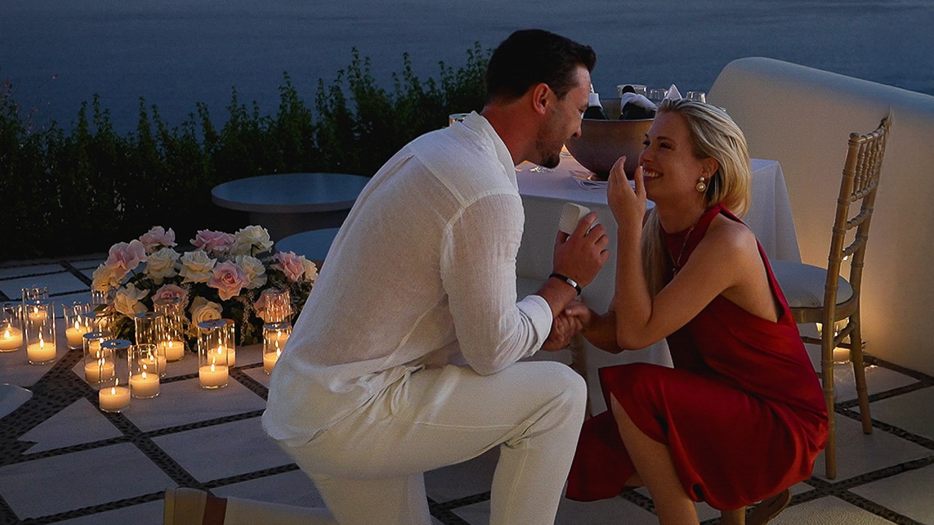 Channing Millerd kneeling on one knee proposing to Eliza Spencer next to a table surrounded by candles and roses