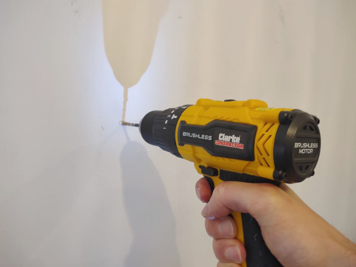 A yellow handheld drill being used on a white wall