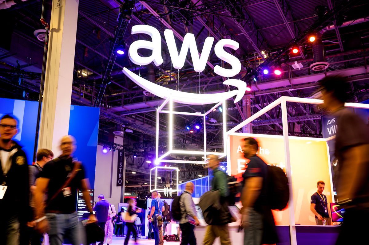 A bright white AWS logo hanging from the ceiling above the busy conference floor of AWS Re:Invent