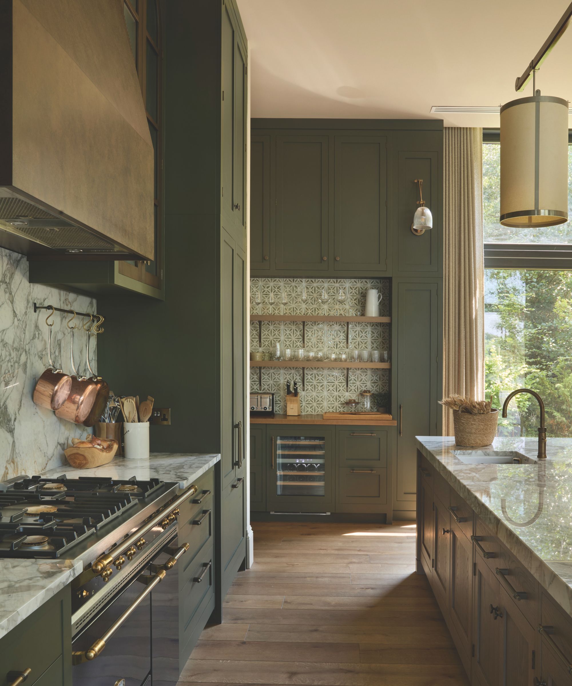 A traditional dark olive green kitchen with floor to ceiling cupboards and a white marble worktop