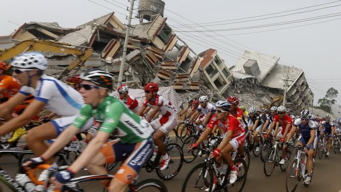 The peloton passes ruined buildings on stage 3