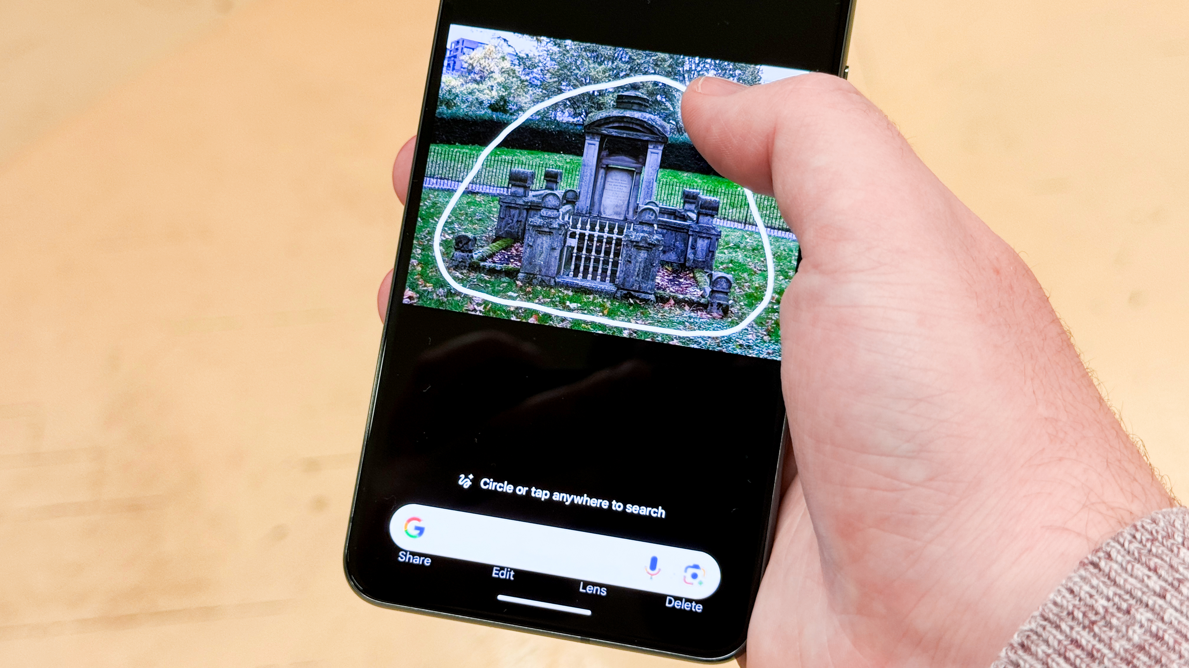 An image of a Pixel being held in a person's hand with the Circle to Search feature being used on the screen to search for a mausoleum.