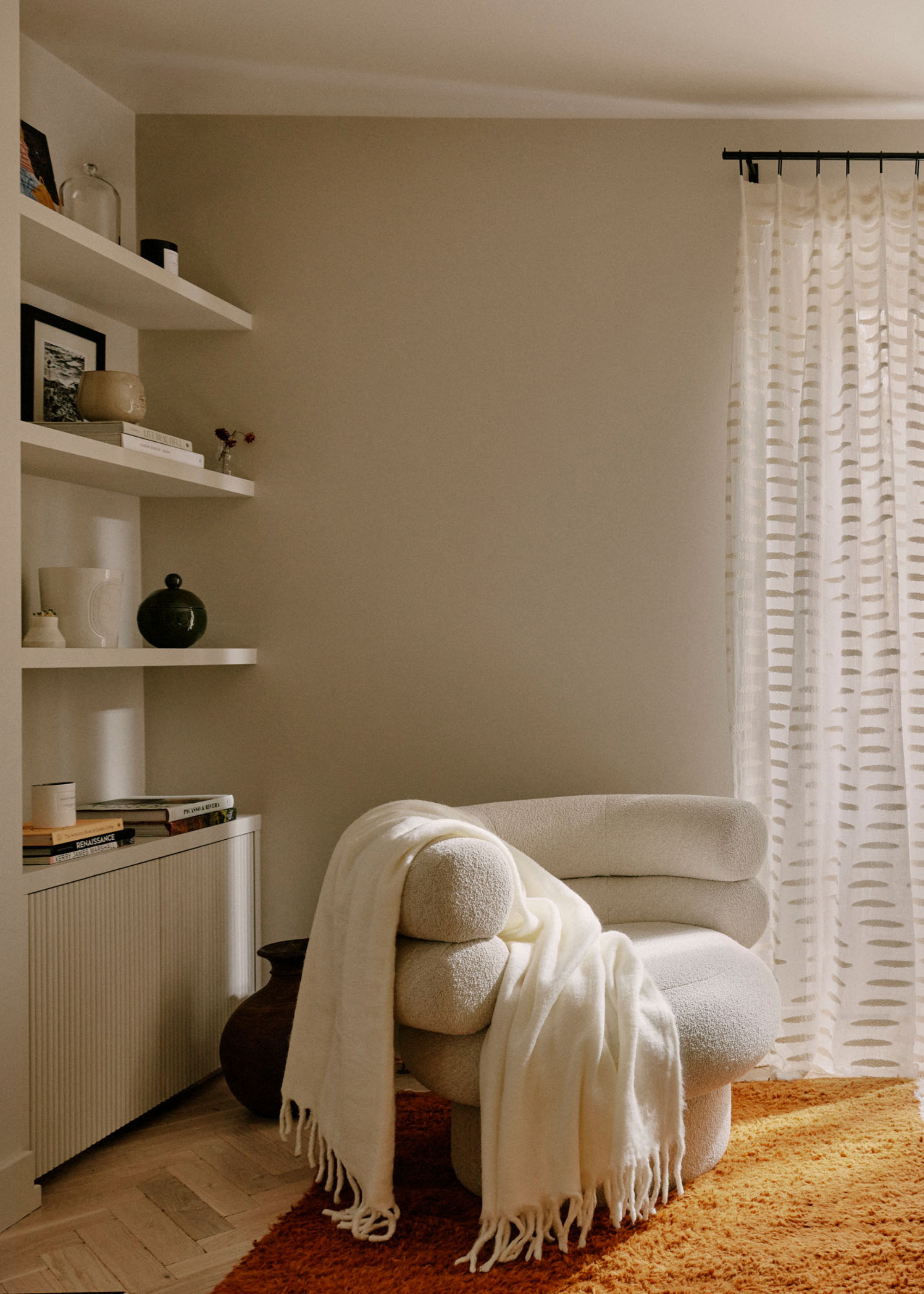A living room with a sofa seater, a white throw, a large area rug and an in-built shelving unit