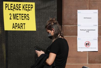 A member of the public queues by a sign reading "Testing by appointment only"