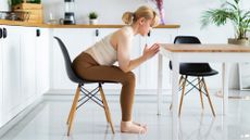 Woman sitting down on chair in kitchen as part of 5-minute workout
