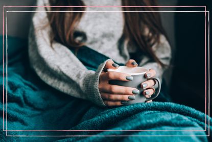 A woman holding a mug of hot green tea, one of the cold remedies recommended by experts