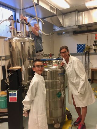 Dr. Karolien Denef and her son, Griffin, assist Dr. Christopher Rithner who is transferring liquid Helium from a cryogenic dewar to a superconducting magnet dewar for NMR. About one-third of helium consumed supports high magnetic field magnets in medical MRI, research NMR, and particle beams.