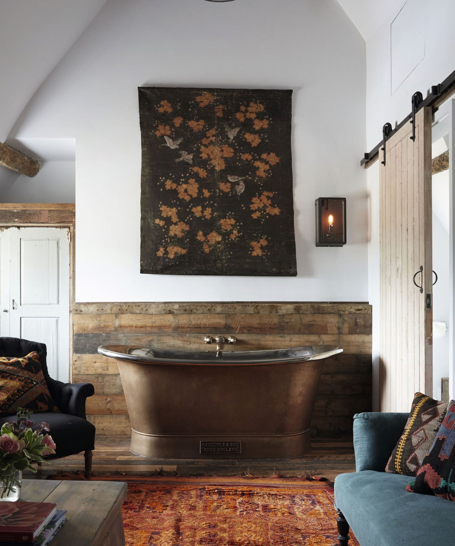 bathroom with rug and wooden paneling on walls and fabric artwork and copper freestanding tub