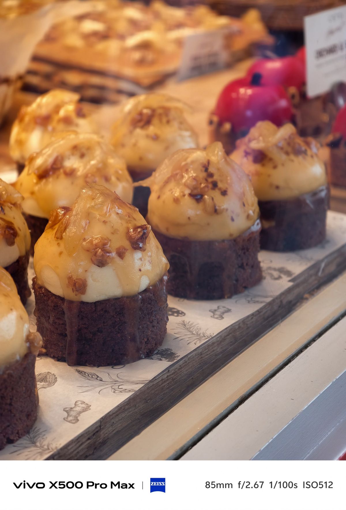 Display of chocolate cakes topped with cream and chopped nuts in a warmly lit bakery window.
