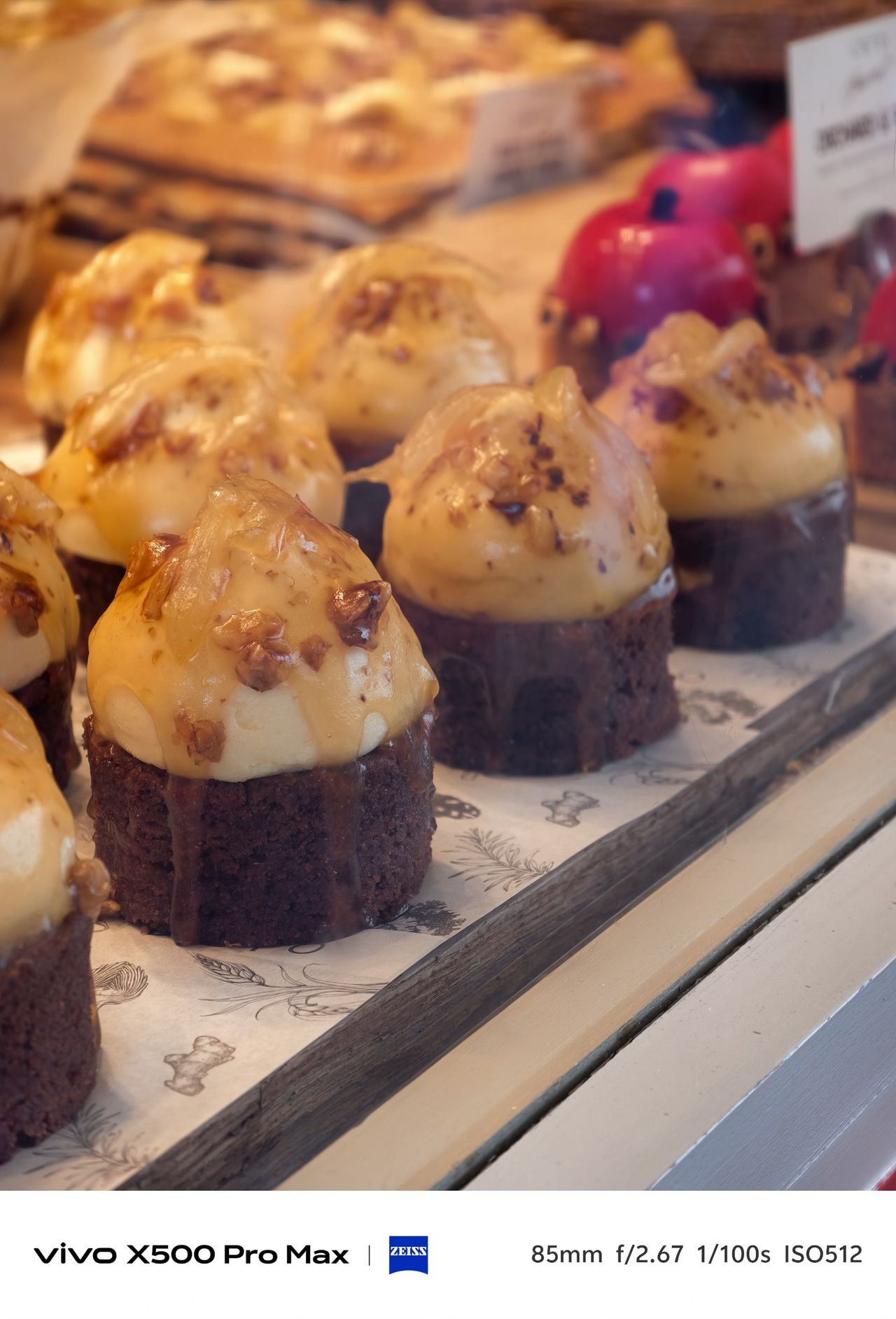 Display of chocolate cakes topped with cream and chopped nuts in a warmly lit bakery window.