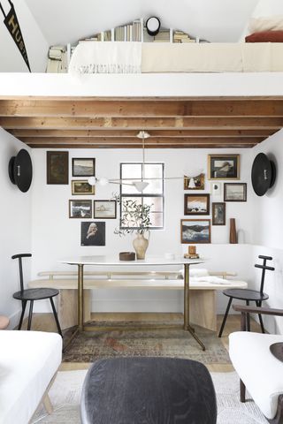 compact living space with dining room, living space, mezzanine floor, all white, gallery wall behind dining table, retro lights, vintage rug, black wood coffee table