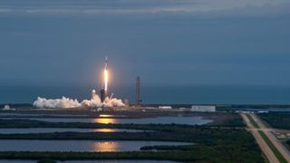 a white and black rocket launching from a seaside pad