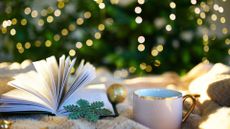 White cup and book against defocused lights on Christmas tree