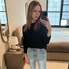 Nikki wears a black sweater with light-wash bootcut jeans.