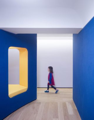 Young girl walks through playroom with bold colours of blue and yellow.