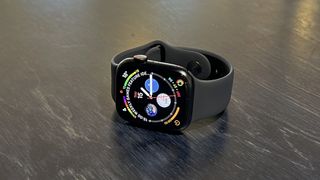 En Apple Watch 8 med en svart silikonrem ligger på et mørkt trebord.