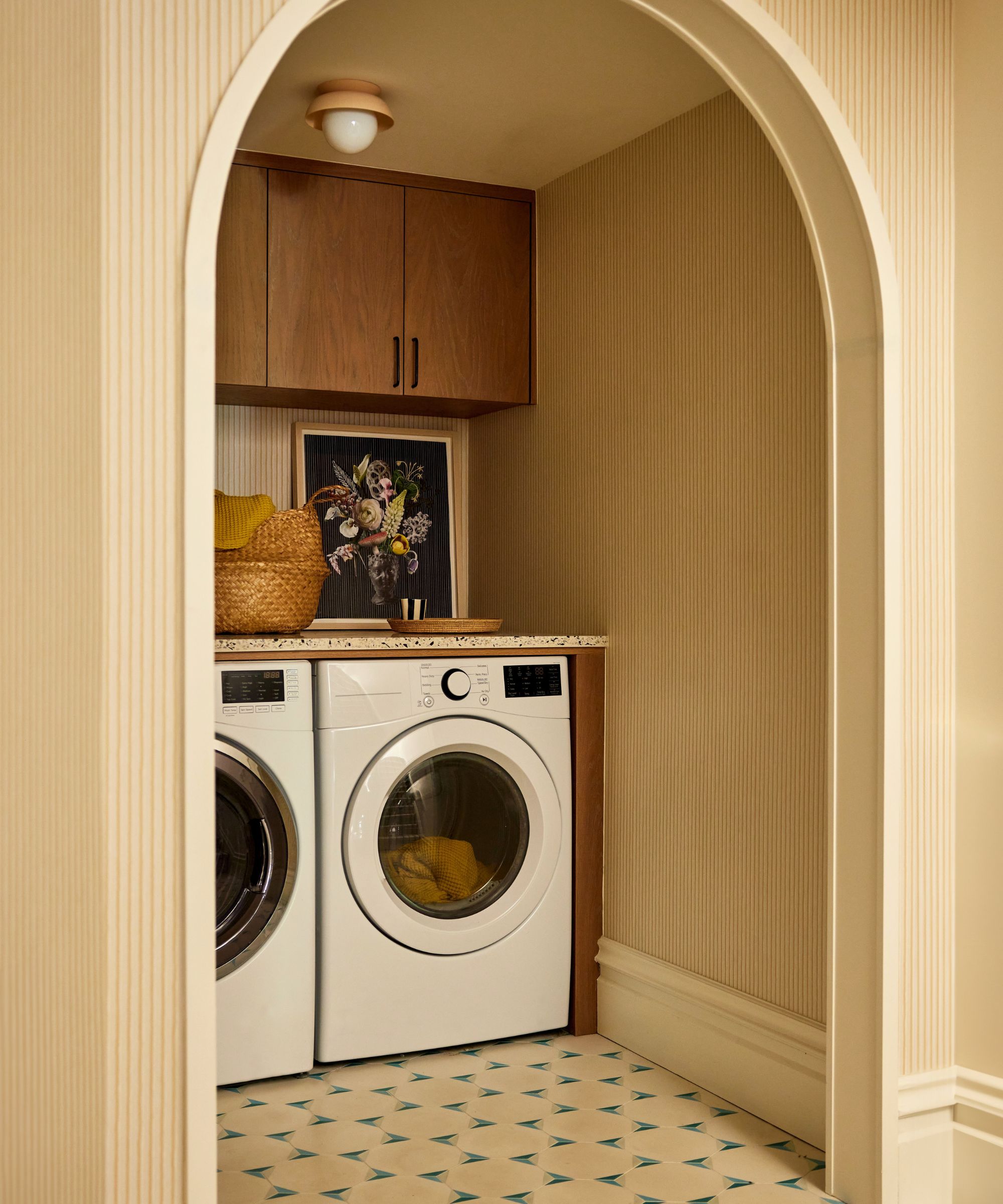 Small nook used as a laundry with wooden cabinets and arched doorway