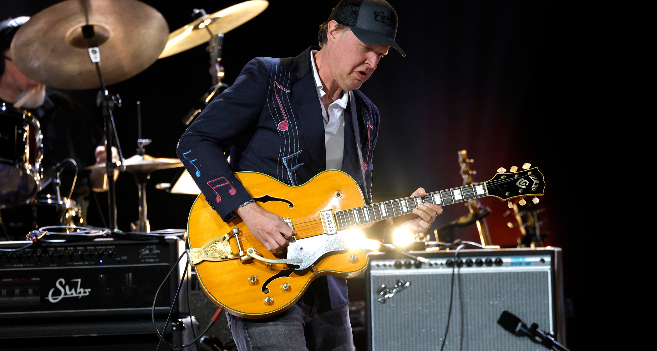 Joe Bonamassa plays a Guild DE-500 Duane Eddy signature guitar at a Nashville show celebrating Eddy&#039;s life. Bonamassa wears a dark blazer embroidered with bright musical notation.