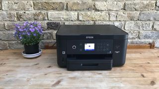 An Epson printer on a wooden table in front of a brick wall