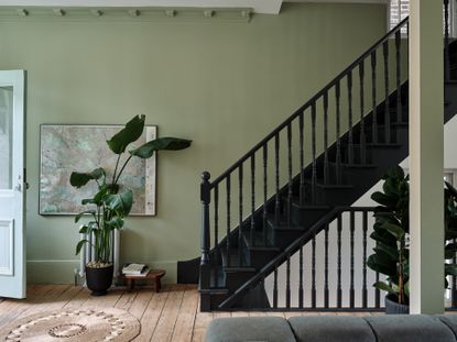 Entryway with green walls, dark wood bannisters and house plants.