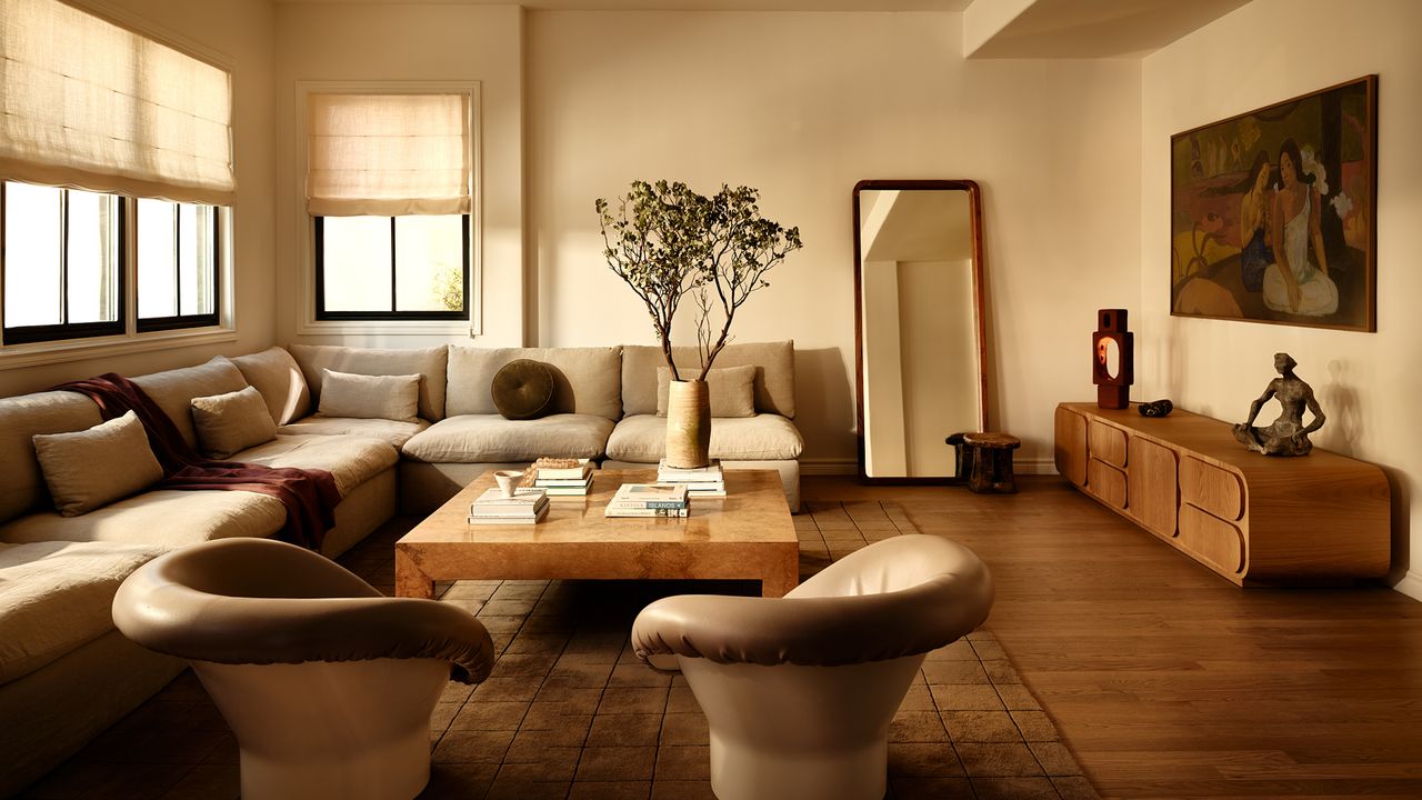 a beige living room with beige furniture, a mirror leant against the wall and a large cut branch in a vase on the coffee table