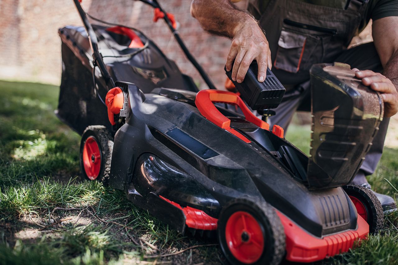 Why we don’t recommend gas lawn mowers - A man adding a cordless mower battery to a lawn mower 