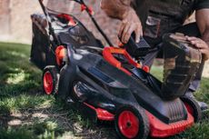 why we don’t recommend gas lawn mowers - a man adding a cordless mower battery to a lawn mower 