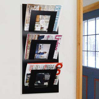 A three tier wall mounted magazine rack in black holding assorted titles.